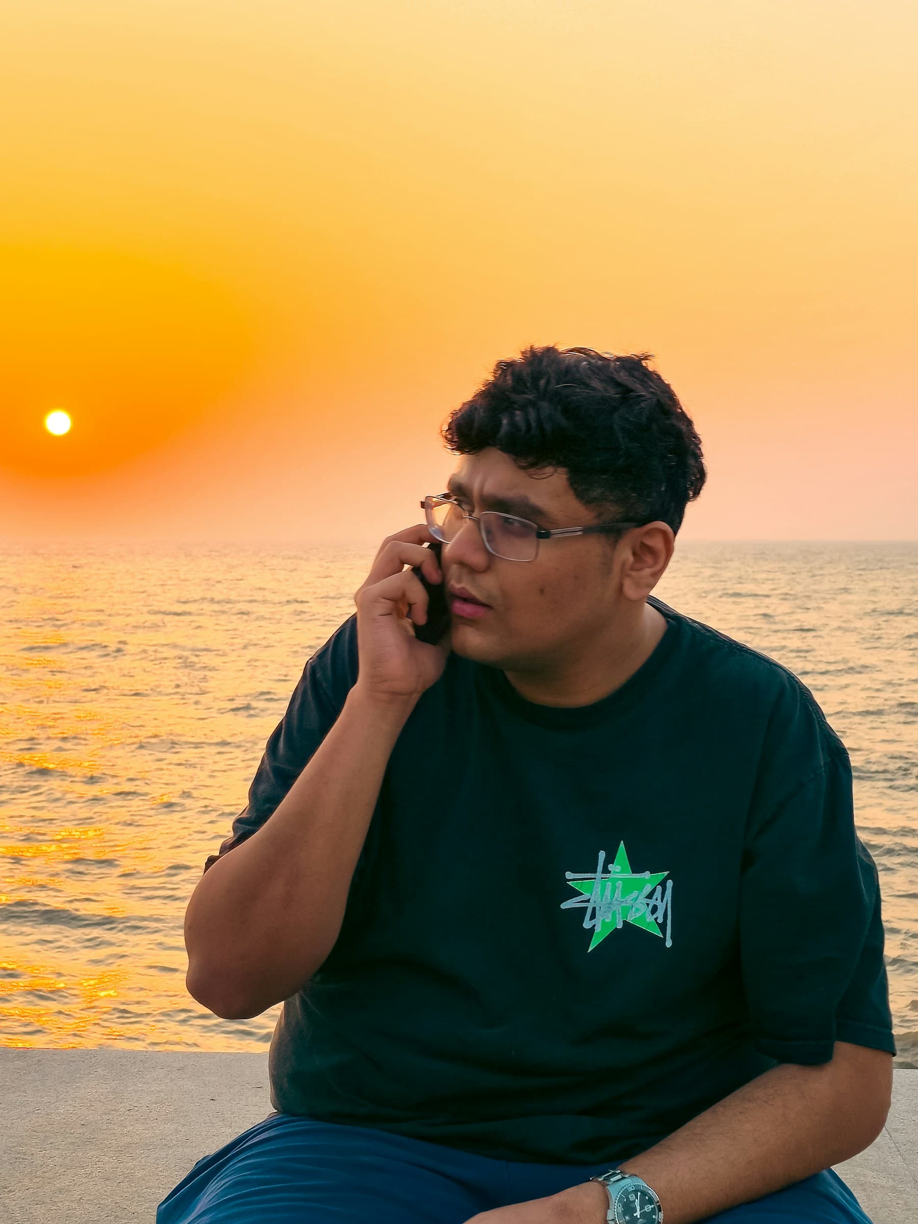 A man having a calm phone conversation by the sea in Mumbai at sunset
